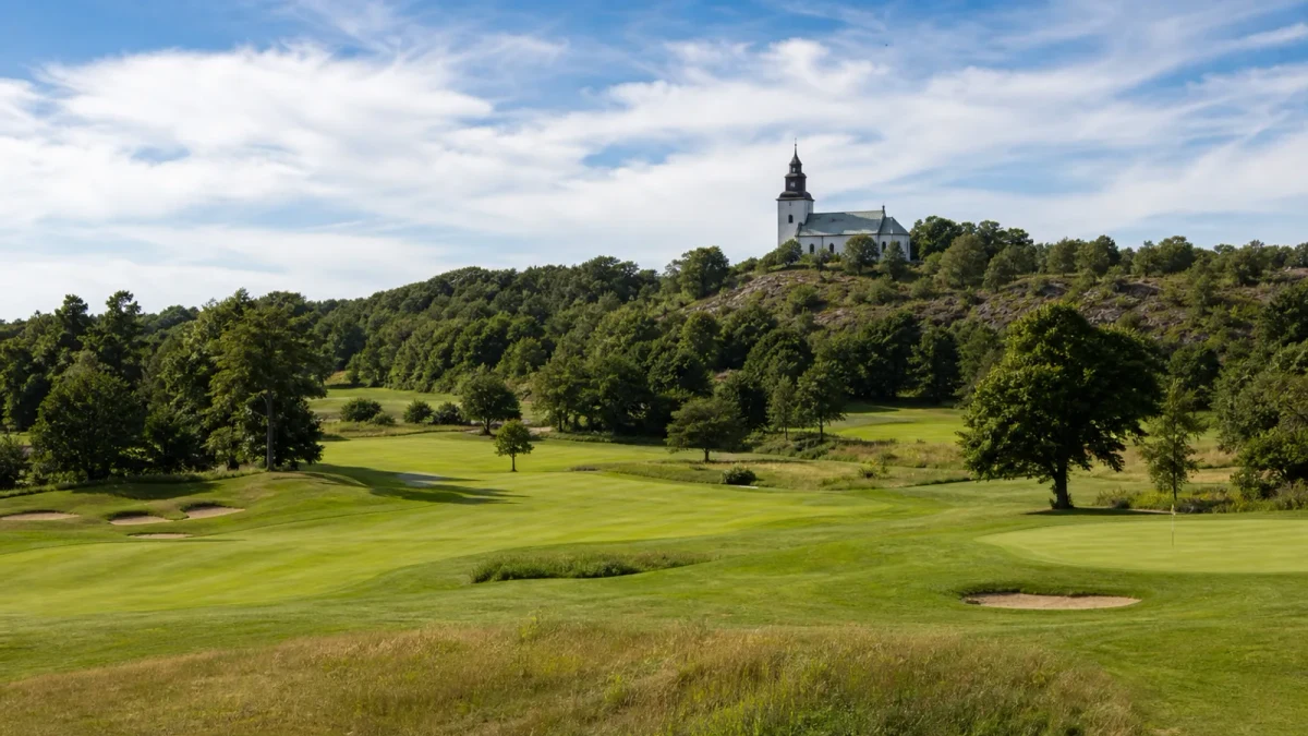 Fairway på en svensk golfbana i kvällsljus med skog och vatten i bakgrunden
